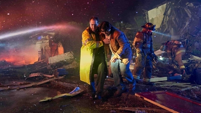 A first responder rescues a tornado victim from the wreckage of a building during the night.