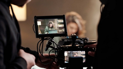 Two videographers focus a camera on a subject.