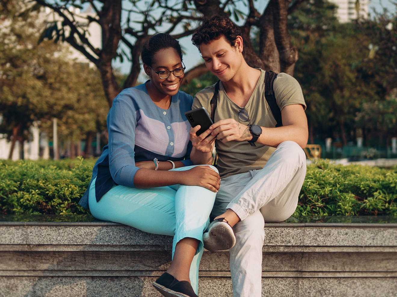 Dos personas sentadas en un parque, mirando un smartphone.