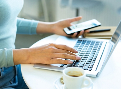 Person using smartphone and laptop in coffee shop.